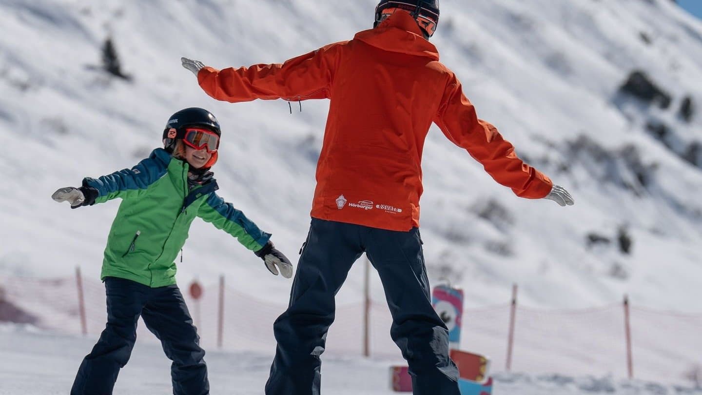 An instructor and a child on skis, arms out for balance