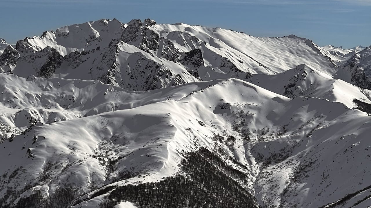 Snow covered jagged peaks seen from above, with no tracks or lift lines in sight