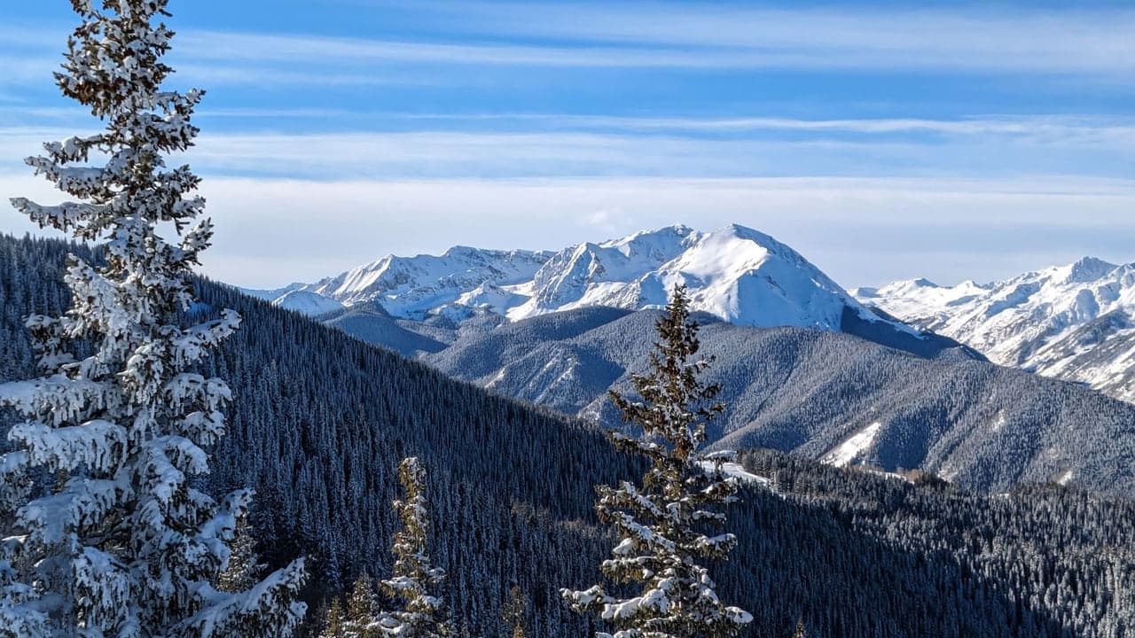Snow covered alpine peaks rising above a forested ridge, the kind of terrain a heli-ski day is built around