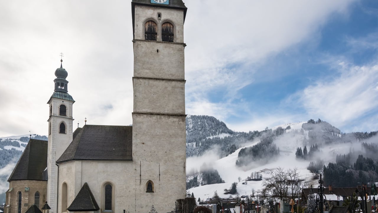 A stone church tower above a snowbound alpine village beneath the mountains