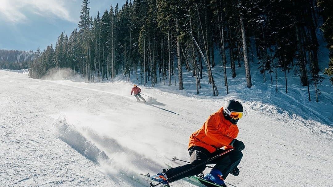 A skier carving a groomed run under a clear blue sky