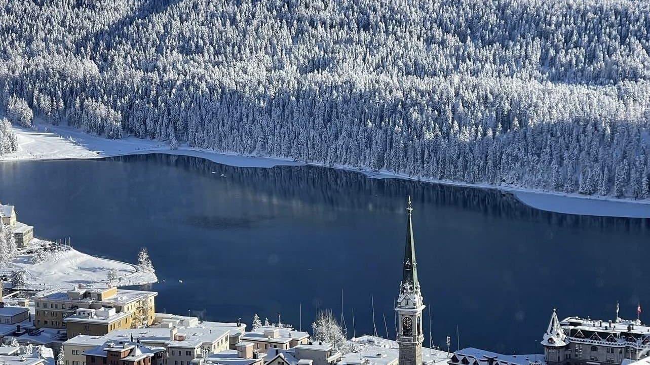 St. Moritz from above, the town and church tower below the frozen lake and the forest