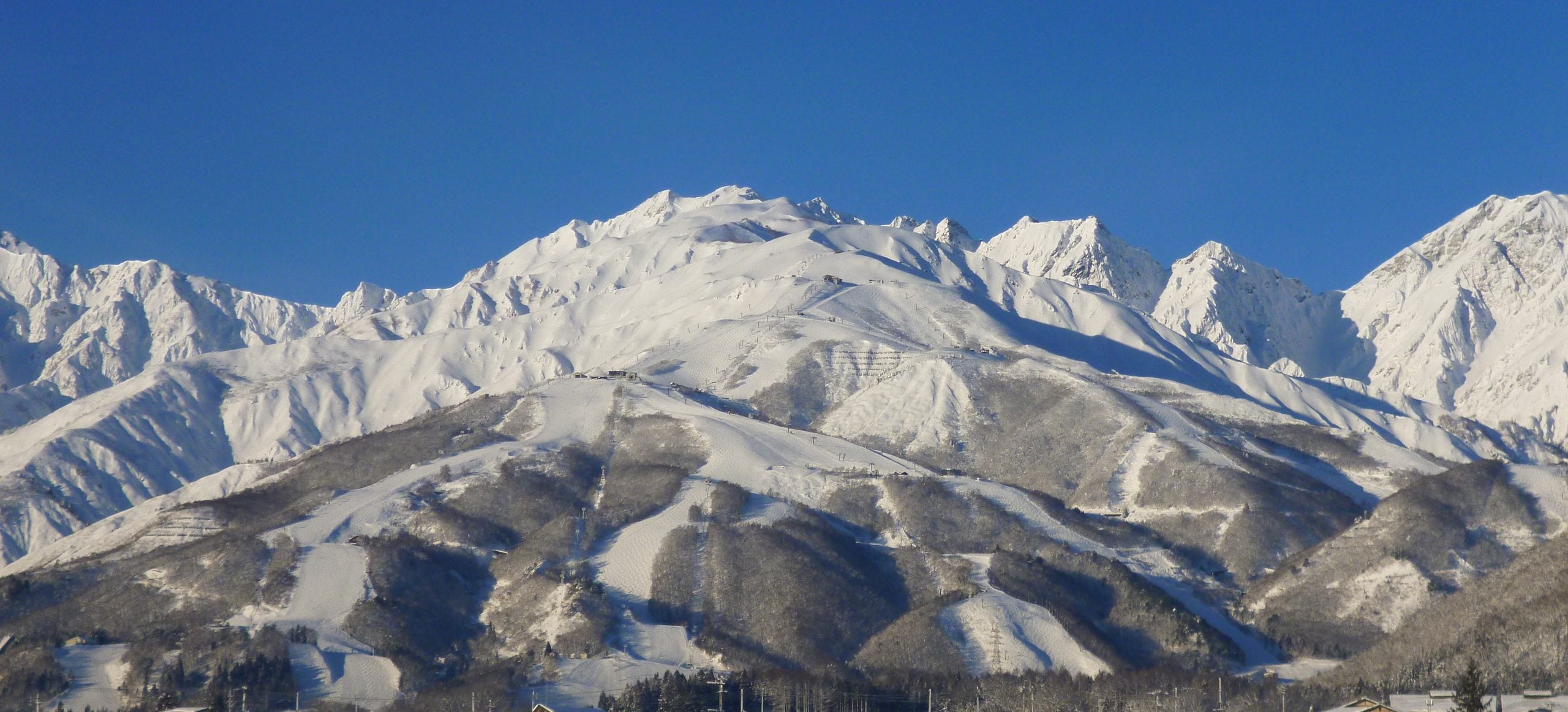The snow covered Hakuba range above the ski runs and the village of Hakuba in Nagano, under a clear winter sky.