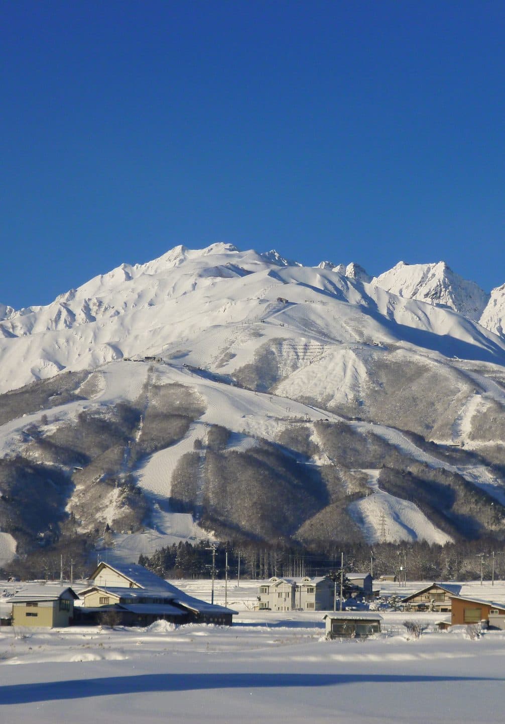 The snow covered Hakuba range above the ski runs and the village of Hakuba in Nagano, under a clear winter sky.